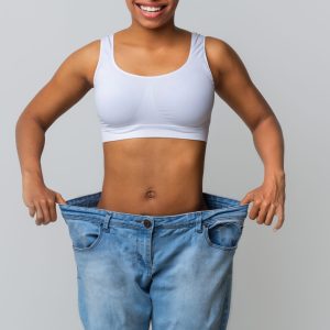 Successful weight loss, afro woman with too large jeans after effective diet, grey background