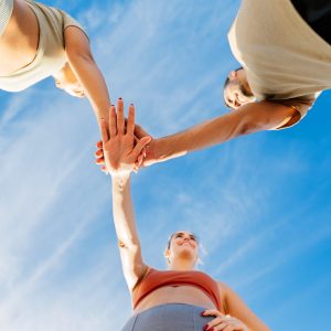 Low angle view of young group of sportive friends in circle stacking hands motivating each other before workout exercise routine in the street. Fitness, sport and teamwork concept. Vertical photo.